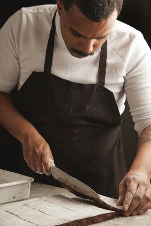 Black man in apron slicing brownies