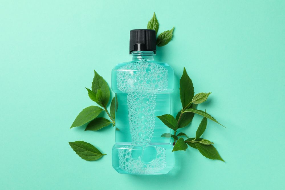 Mouthwash and leaves on mint background, space for text