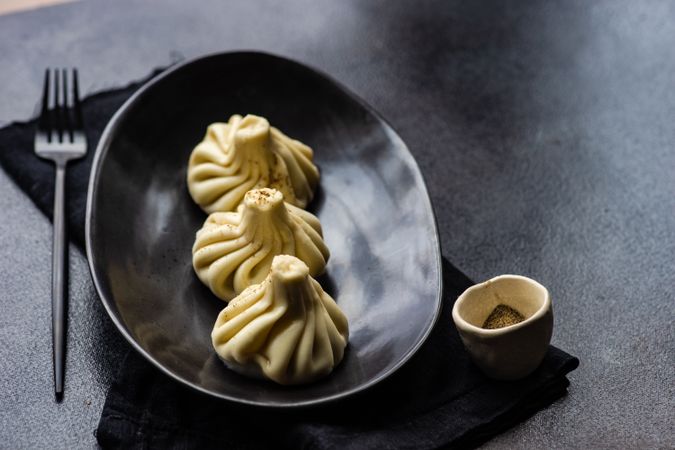 Plate of three Georgian khinkali dumplings on dark plate and table