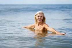 Mature woman in bathing in the sea with open arms