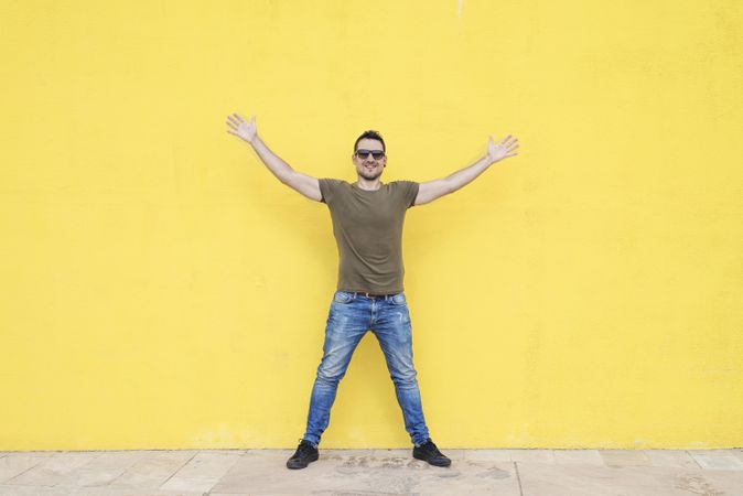 Happy male standing outside in front of yellow wall with open arms
