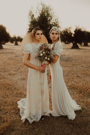 Charming slim brides with flowers in garden with olive trees