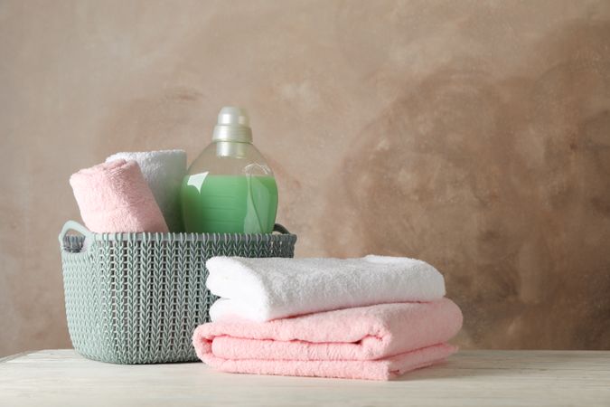 Basket with clean towels and laundry liquid on wooden background, space for text