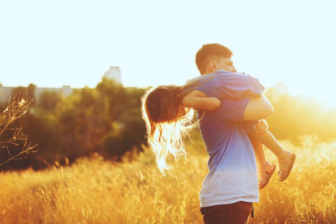 Man carrying daughter on his back through field