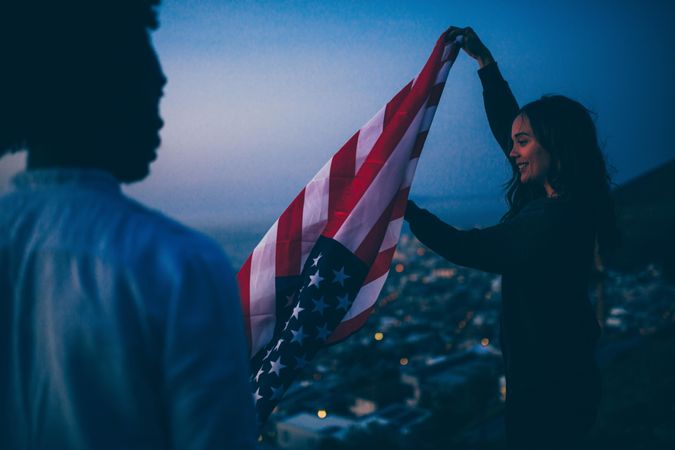 A smiling woman unfolding the American flag at dusk with friend