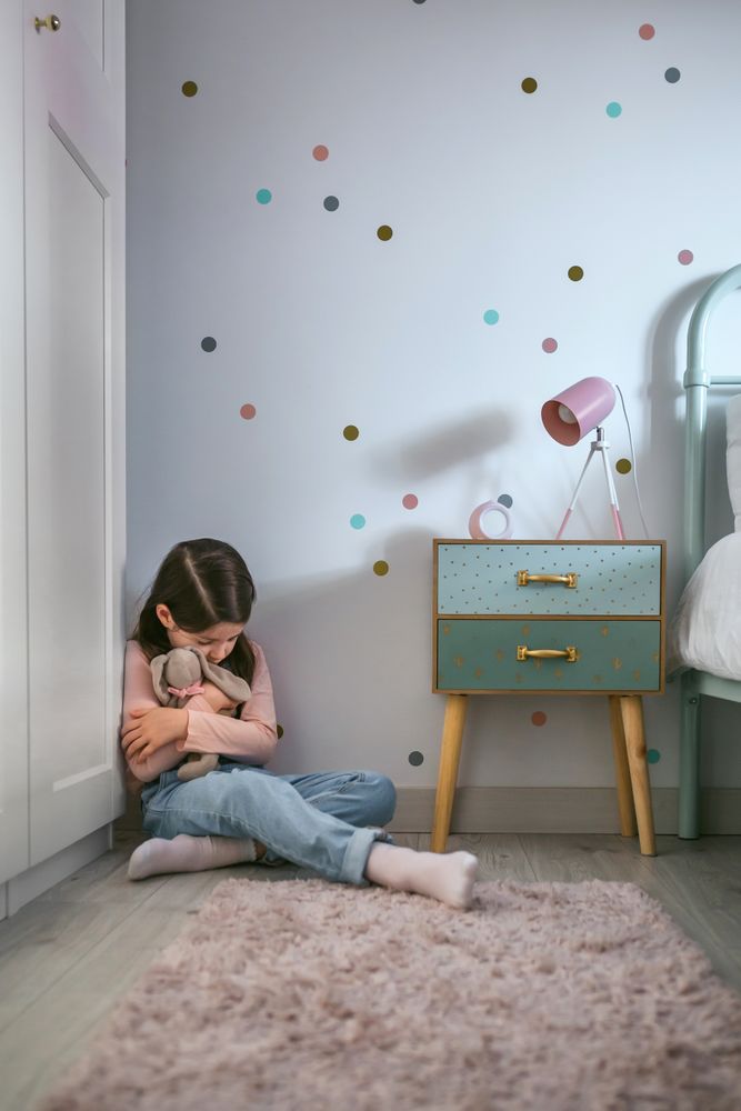 Depressed girl hugging plush doll sitting on the floor