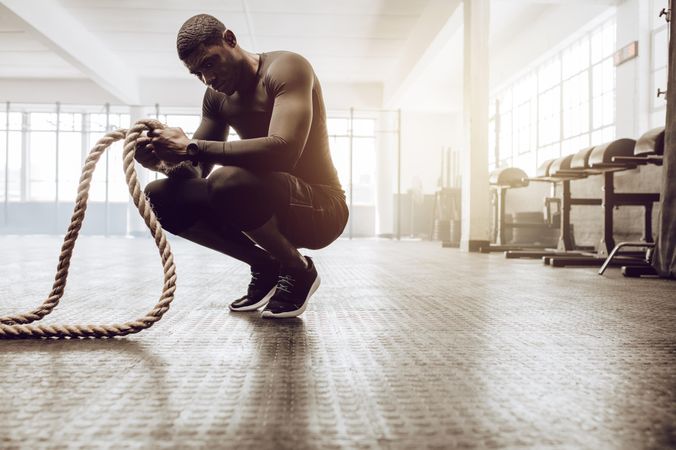 Man sitting on his toes holding a pair of battle ropes for workout