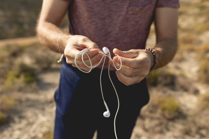 A man untangles the cable of a pair of headphones to listen to music during a walk in the countryside