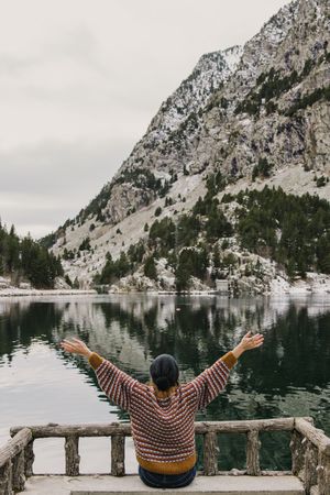 Woman on seat near wonderful lake between hills in snow and cloudy sky