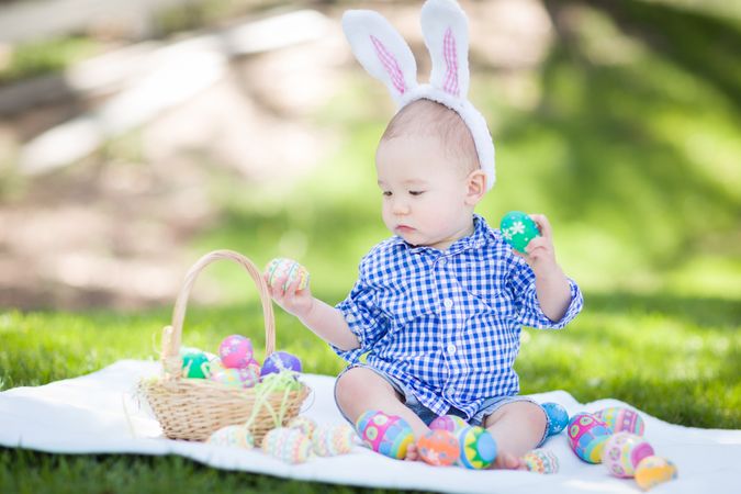 Biracial Baby Outside In Rabbit Ears Playing with Easter Eggs
