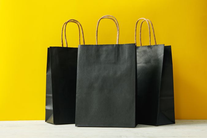 Paper bags on wooden table against yellow background
