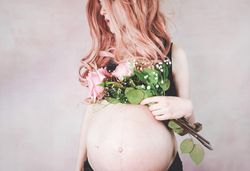 Pregnant woman with pink hair wearing crop top holding pink rose bouquet
