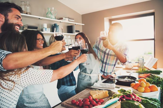 Happy friends toasting with red wine as they cook together at a dinner party