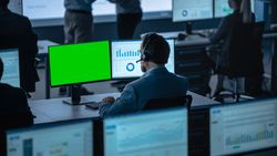 Data Analyst With Headset Examines Financial Charts on Dual Monitors.