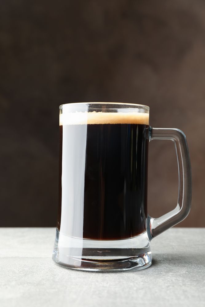 Glass of dark beer on grey table, space for text