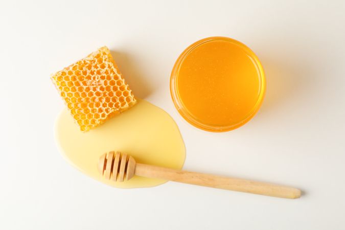 Honeycomb, dipper and jar with honey on neutral background, top view