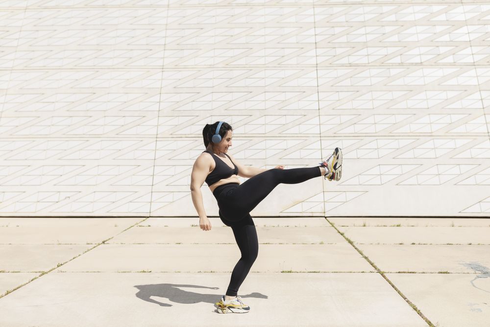 A woman kicks her leg in the air while enjoying some time in the sun after exercising