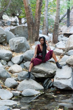 Woman in red velvet outfit in the mountains sitting on boulders