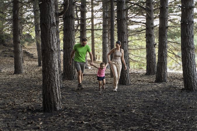 Young family walking through forest holding hands enjoying nature together