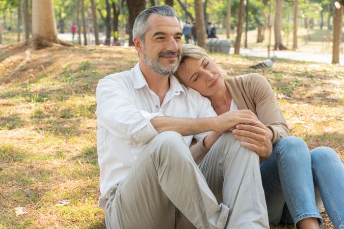 Calm mature woman leaning her head on man’s shoulder while sitting in park