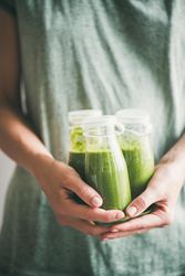 Woman in green dress holding three bottles of green smoothie
