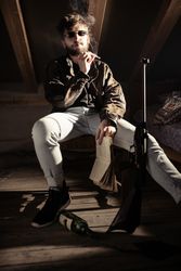 Man in eyeglasses smoking cigarette near bottle and gun