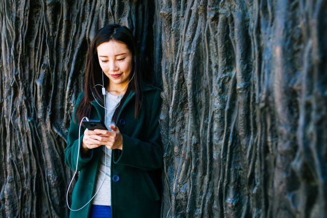 Asian female listening to music near rough wall
