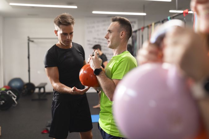 A trainer assists trainee performing squats with the kettlebell