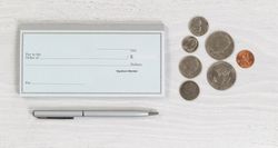 Blank checkbook with pen and coins on desktop