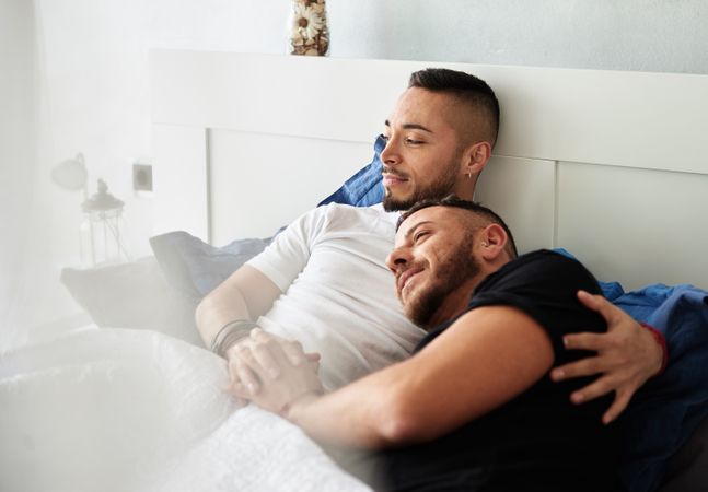 Smiling gay couple hugging on bed