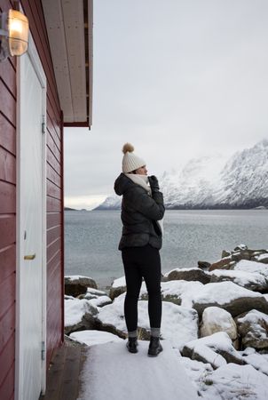 Solitary woman on rocky shore against tranquil lake and snowy mountains in cold day
