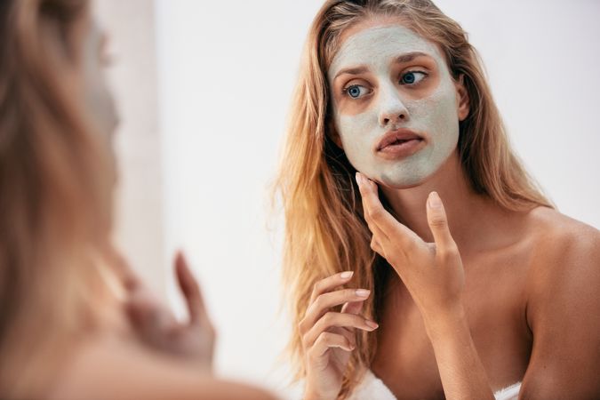 Woman looking in the mirror with mask on her face