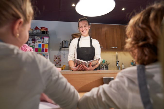 Cheerful young woman standing at counter and reading for anonymo