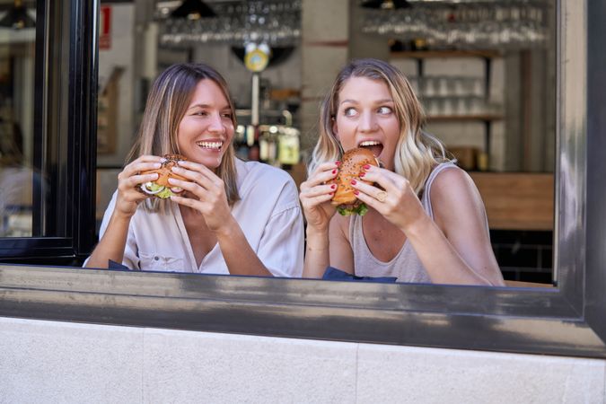 Happy women eating burgers together in cafe