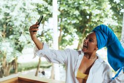 Positive woman with turban on head taking selfie on sunny street