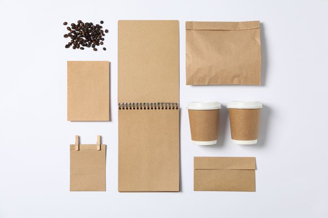 Flat lay. Blank stationery, paper cups and bunch of coffee on plain background, mockup