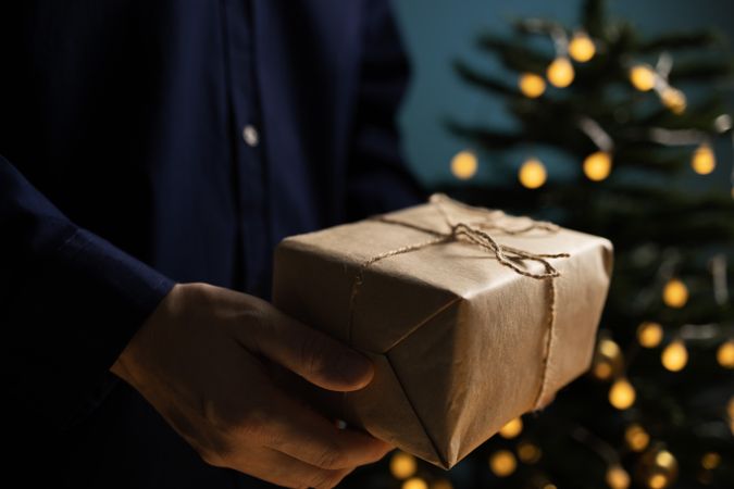 Man holding Christmas gift near tree