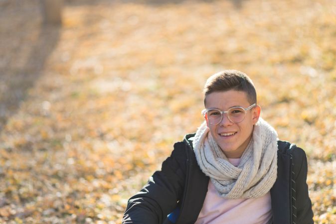 Smiling teenage male in striking eyewear sitting on grass in a city park
