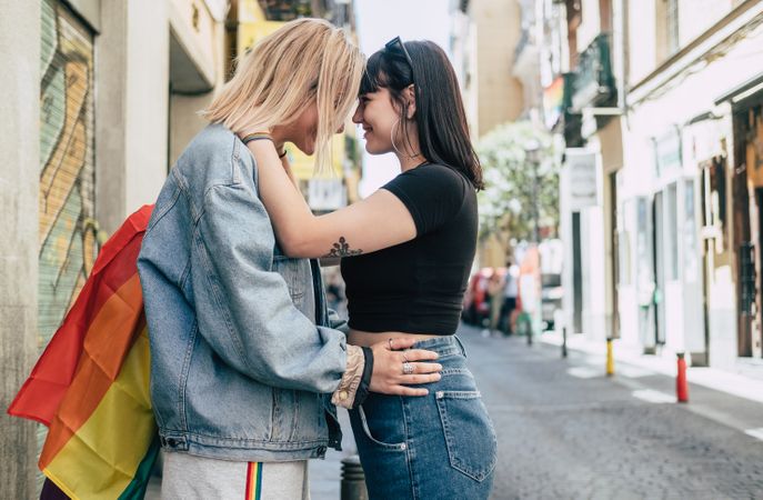 Lesbian couple with LGBT flag standing on street