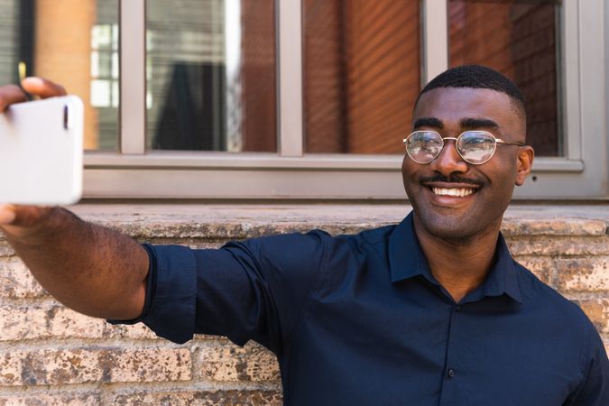 Smiling Black man taking selfie on smartphone near building