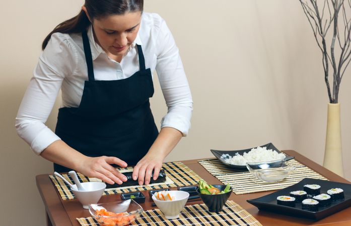 Female chef in apron rolling sushi rolls on table