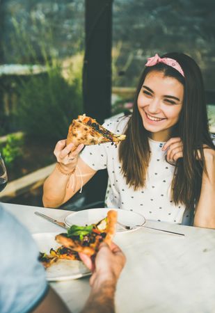 Couple eating pizza al fresco with wine with woman smiling holding pizza