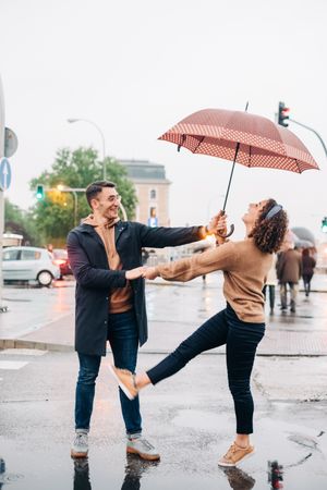 Happy couple with umbrella hugging on wet street