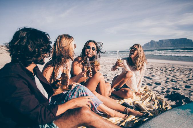 Smiling group of friends sitting on the beach enjoying drinks