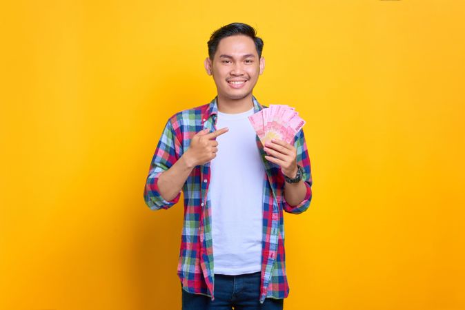 Smiling Asian man holding up cash and pointing to it in studio shoot