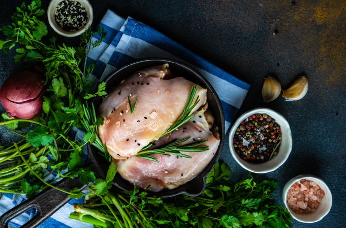 Top view of raw chicken with rosemary sprig on kitchen slab with seasoning