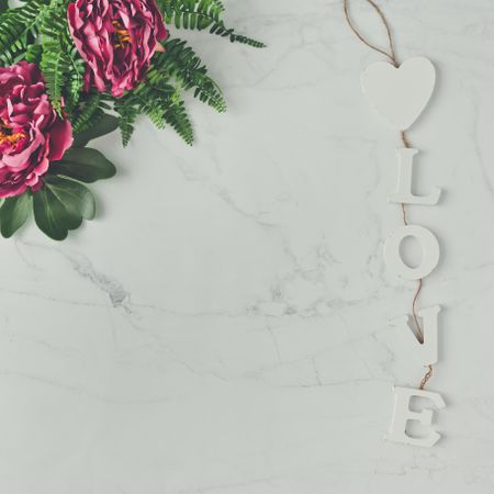 Pink flowers and leaves on marble background with the word “Love”