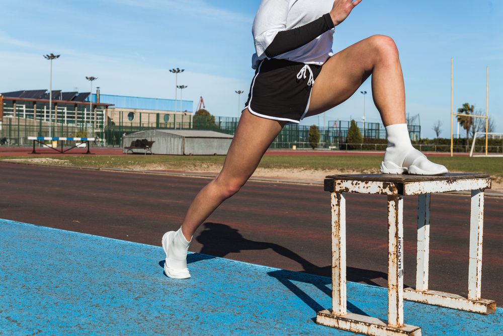 Female athlete stretching on stool on stadium