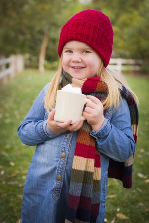 Cute Young Girl Holding Cocoa Mug with Marsh Mallows Outside