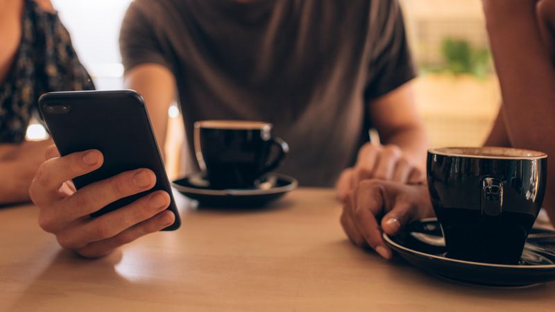 Close up of a smartphone being used by a man sitting at a cafe table with his friends